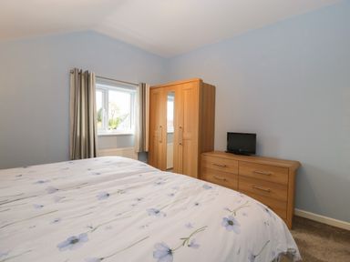 A bedroom with a bed covered in floral bedding a wooden wardrobe and a wooden dresser with a small television at The Cider Shed in Winscombe