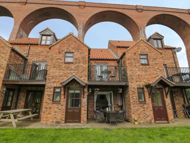 A brick house with balconies outdoor seating and large brick arches above at Maplebeck in Whitby