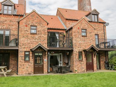 A brick building with two balconies and a patio area with outdoor furniture at Maplebeck Whitby