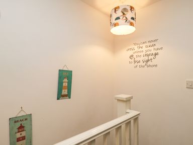 A stairwell with white walls and a handrail with seaside-themed wall art and a hanging lamp at Maplebeck in Whitby