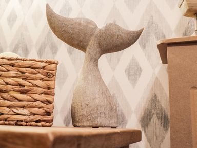 A wooden whale tail sculpture on a wooden shelf with a woven basket and diamond patterned wallpaper at Maplebeck in Whitby