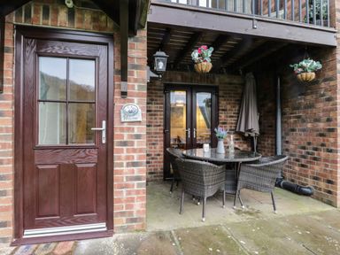 An outdoor patio area with a round table and wicker chairs under a wooden balcony at Maplebeck in Whitby