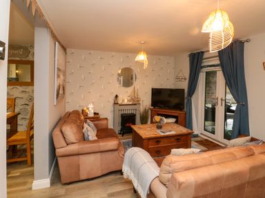 A living room with two brown sofas a wooden coffee table a TV on a wooden stand and blue curtains at Maplebeck in Whitby