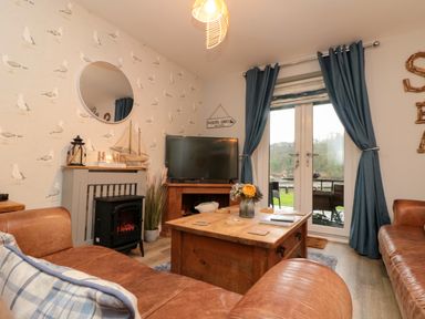 A living room with brown leather sofas a wooden coffee table and a television near blue curtains and a fireplace at Maplebeck in Whitby