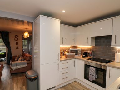 A kitchen with white cabinets black oven and microwave next to a living room with brown sofas at Maplebeck Whitby