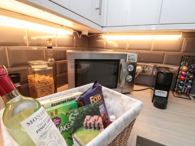 A kitchen countertop with a microwave coffee machine glass jar of pasta and a basket with snacks and wine at Maplebeck in Whitby