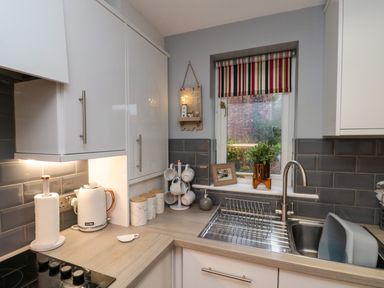 A kitchen corner with countertop, kettle, paper towel holder, mugs on a rack, sink, and window with striped blind at Maplebeck in Whitby