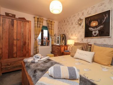 A bedroom with a wooden wardrobe bed with cushions and blankets a wooden dresser window with yellow plaid curtains and deer artwork on the wall at Maplebeck in Whitby