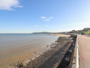 A beachfront promenade with a rocky shore and calm sea at Puffin View in Rhos-On-Sea