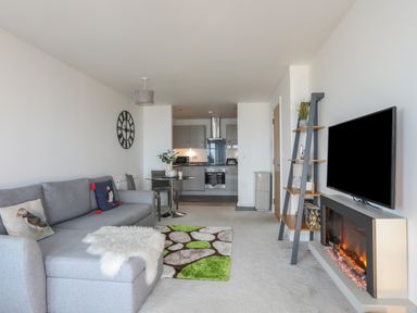 An open plan living room and kitchen with a grey sofa and cushions and a round table at Puffin View in Rhos-On-Sea
