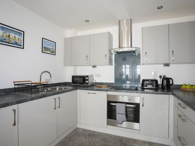 A kitchen with gray cabinets black countertop stainless steel oven microwave toaster kettle and a fruit basket at Puffin View in Rhos-On-Sea