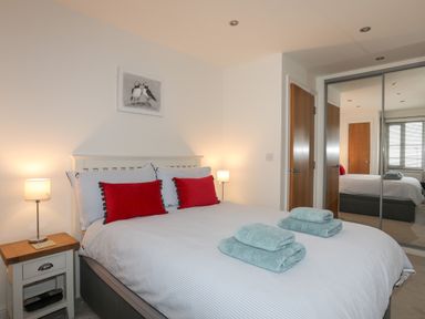 A bedroom with a bed with red pillows and folded towels on top at Puffin View in Rhos-On-Sea