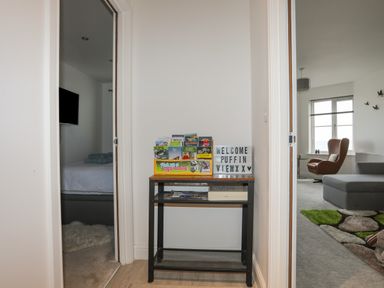 A hallway with a small table holding brochures and a welcome sign between a bedroom and a living room at Puffin View in Rhos-On-Sea