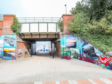A pedestrian underpass with painted murals on brick walls leading towards a waterfront at Puffin View in Rhos On Sea