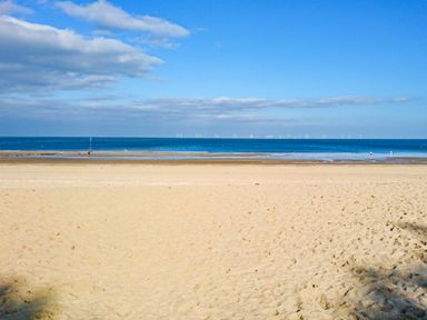 A sandy beach with a calm sea and a blue sky with some clouds