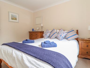 A bedroom with a double bed with blue and patterned pillows two wooden bedside cabinets and framed pictures on the walls at Deja Blue in Falmouth