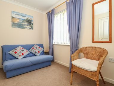 A room with a blue sofa with two patterned cushions a wicker chair with a white cushion a window with blue curtains and a wall mirror at Deja Blue in Falmouth