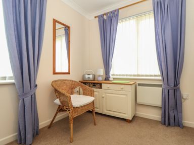A corner room with a wicker chair beside a cabinet with a radio lamp and blue curtains at Deja Blue in Falmouth