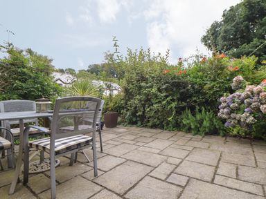 An outdoor patio with metal chairs and a table surrounded by plants and flowers at Deja Blue in Falmouth