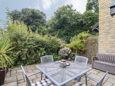 A garden patio with a metal table and chairs surrounded by plants and bushes at Deja Blue in Falmouth