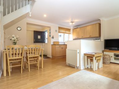 A kitchen and dining area with a wooden dining table and chairs a small television on a cabinet and nested wooden tables at Deja Blue in Falmouth