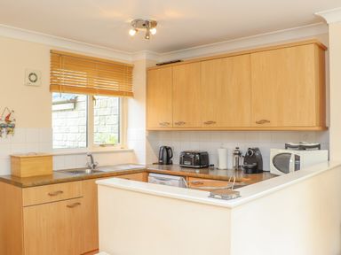 A kitchen with wooden cabinets a sink a toaster a kettle a coffee machine and a microwave at Deja Blue in Falmouth