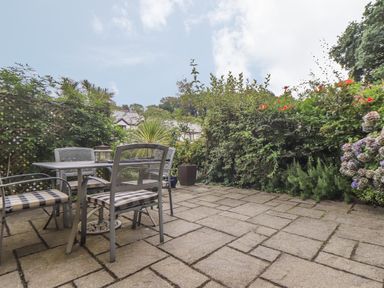 An outdoor patio area with a metal table and four chairs surrounded by plants at Deja Blue in Falmouth