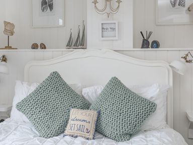 A bed with two large knitted cushions and a small decorative cushion on white bedding at The Old Boat Store in Morfa Nefyn