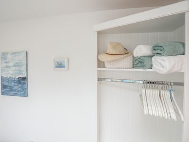 A closet with folded towels a straw hat and white hangers on a rail with paintings on the wall at The Old Boat Store in Morfa Nefyn