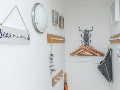 A hallway corner with wooden coat hangers on a decorative metal hook and wooden pegs on the walls at The Old Boat Store in Morfa Nefyn