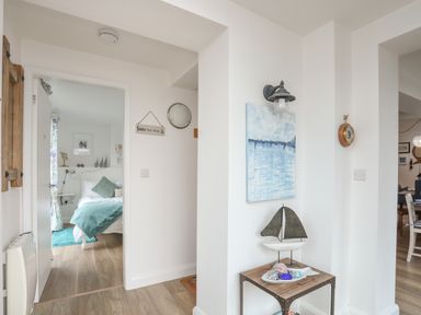 A hallway with a small table and nautical decorations and a view into a bedroom with a bed and blanket at The Old Boat Store in Morfa Nefyn