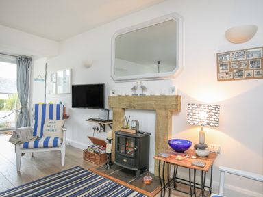 A living room with a striped chair a wood stove and a TV on the wall at The Old Boat Store in Morfa Nefyn