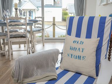 A striped armchair with a cushion and blanket next to a dining table with chairs in a room at The Old Boat Store in Morfa Nefyn