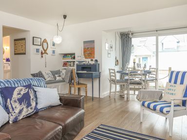 A living room with a brown leather sofa striped cushions a small dining table with chairs and a blue desk with books and decorations at The Old Boat Store in Morfa Nefyn