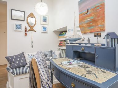 A corner with a blue desk and striped cushions on a built-in bench with framed pictures on the wall at The Old Boat Store in Morfa Nefyn