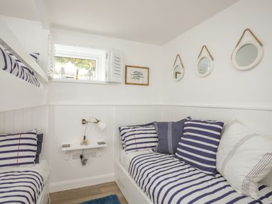 A small bedroom with bunk beds striped bedding three round mirrors on the wall and a small window at The Old Boat Store in Morfa Nefyn