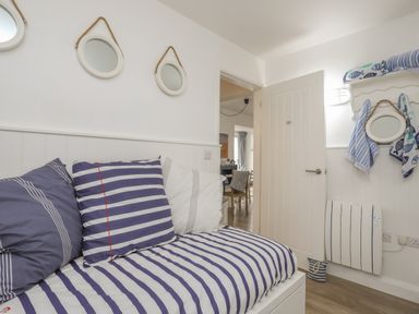 A small room with striped bedding and pillows a door a wall heater mirrors and towels at The Old Boat Store in Morfa Nefyn