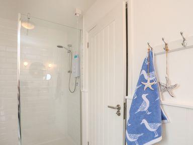 A bathroom with a glass shower enclosure a door and hooks with a blue towel and starfish decorations at The Old Boat Store in Morfa Nefyn