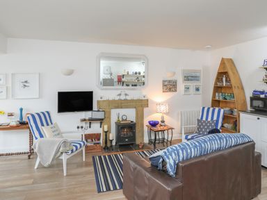 A living room with striped chairs a wooden shelf shaped like a boat and a wall-mounted television at The Old Boat Store in Morfa Nefyn