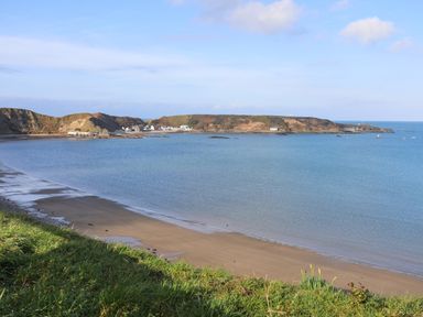 A small bay with sandy beach grassy foreground calm sea and buildings on distant shore at The Old Boat Store in Morfa Nefyn
