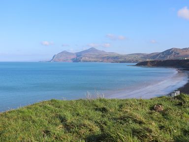 A coastal landscape with a grassy foreground a sandy beach a blue sea and hills in the background at The Old Boat Store in Morfa Nefyn