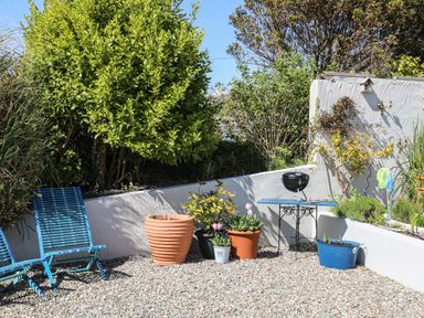 A garden area with blue chairs potted plants a small table and a barbeque at The Old Boat Store in Morfa Nefyn