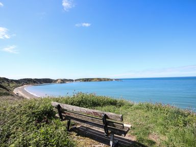A bench on a grassy hill overlooking a bay with a sandy beach and clear blue sky at The Old Boat Store in Morfa Nefyn