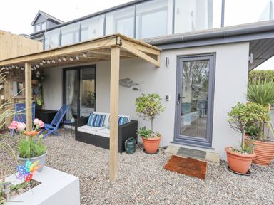 An outdoor patio area with chairs, a sofa, potted plants, and a wooden pergola at The Old Boat Store Morfa Nefyn