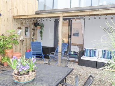 An outdoor patio with metal table and chairs blue chairs and a sofa with striped cushions at The Old Boat Store in Morfa Nefyn