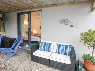 A covered patio with black wicker sofa with striped cushions blue chairs small table and potted plant at The Old Boat Store in Morfa Nefyn