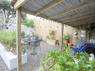 A covered outdoor patio with chairs a table potted plants and gravel flooring at The Old Boat Store in Morfa Nefyn