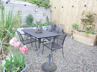 An outdoor patio area with a metal table and chairs on gravel with potted plants and wooden fencing at The Old Boat Store Morfa Nefyn