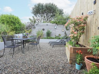 An outdoor patio with a metal table and chairs two lounge chairs plants and a wooden fence at The Old Boat Store in Morfa Nefyn