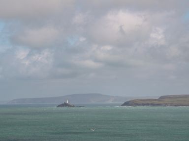 A seascape with a distant lighthouse on a small rocky island and coastal cliffs in the background at Little Valley View in Angarrack